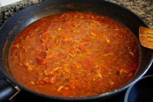 A sofrito saucce simmers on a stove top