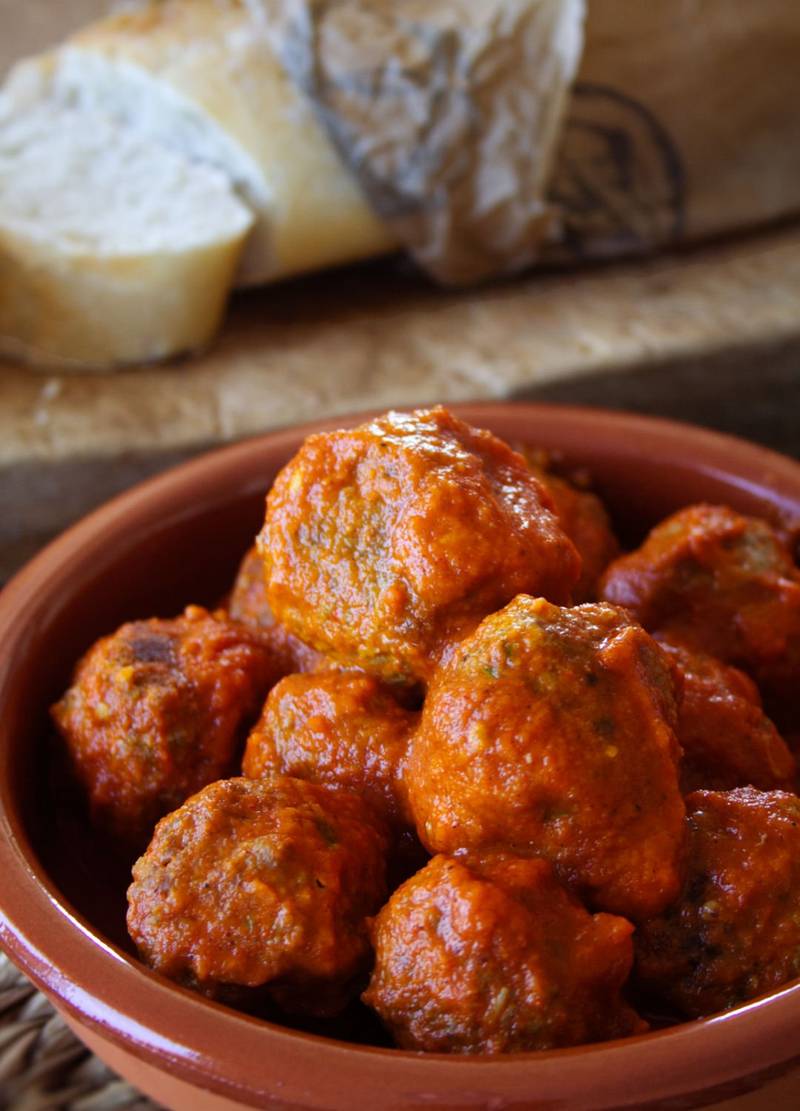 A ceramic. bowl of albondigas sits beside a few slices of fresh bread