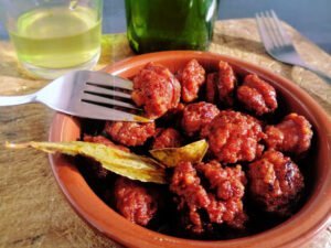 A small earthenware dish sits with a tapas serving of chorizo cooked in cider