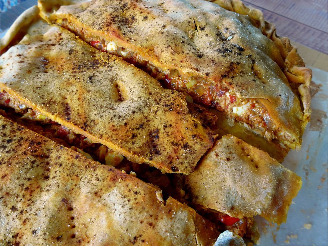 a large tuna empanada sits sliced into pieces on a granite benchtop