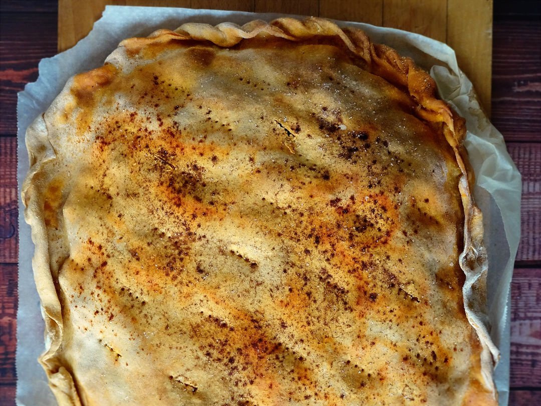 An empanada gallega sits on a chopping board waiting to be cut and served