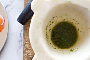 A large white marble mortar sits with some homemade green pesto in the bottom.