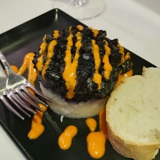 morcilla fiduea is served on a black plate and garnished with a rich red sauce. 