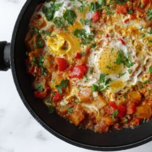 A frying pan of pisto with eggs with a little chopped parsley to garnish