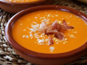 a small bowl of salmorejo is garnished with some diced egg and serrano ham.