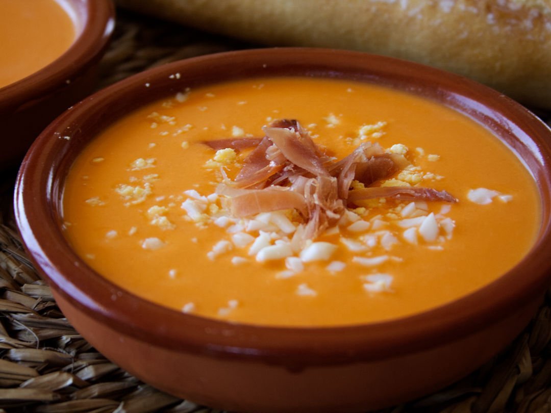 a small bowl of salmorejo is garnished with some diced egg and serrano ham.