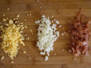 some diced egg white and yolk sit beside some diced serrano ham on a cchopping board