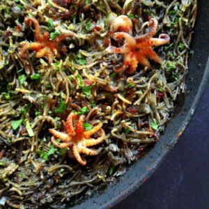 a close up photo of a pan full of fideua negra with baby squid sitting on top