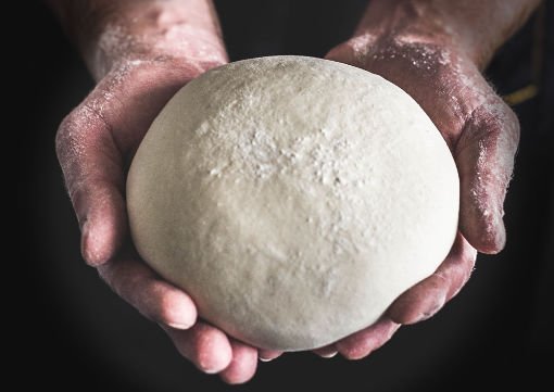 A small ball of vegan dough is cradled in a baker's hands