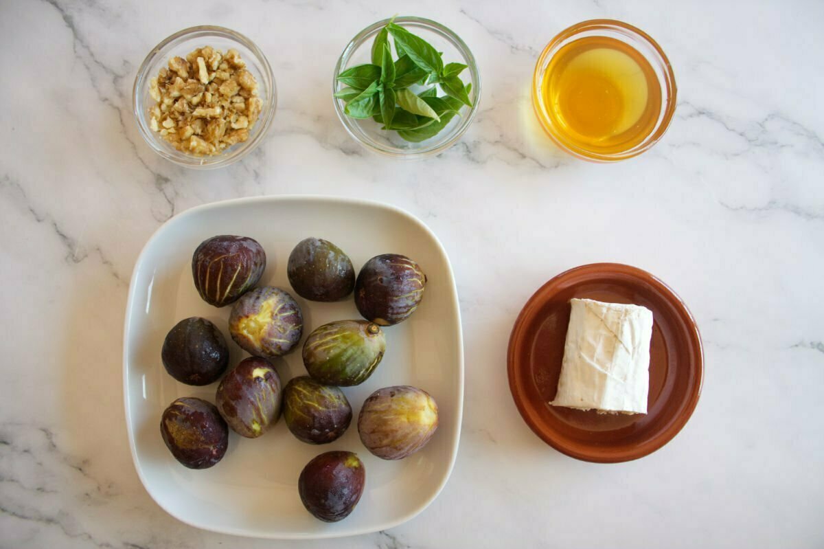 Ingredients to make grilled figs with goats cheese sit on a white marble table