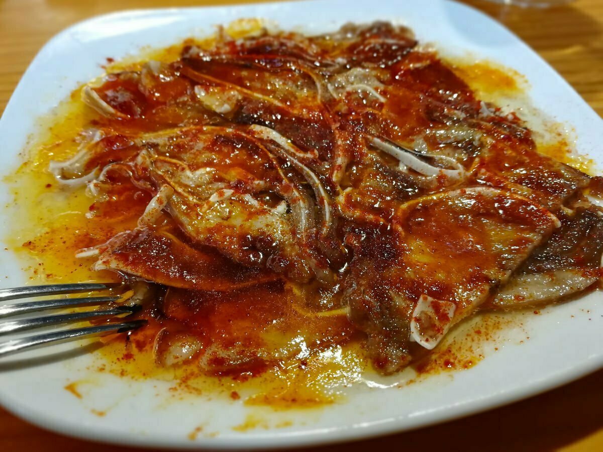 A plate of grilled pork ear sits garnished with some oil and paprika