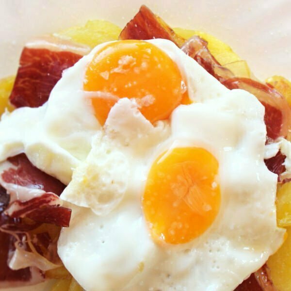 A plate of huevos estrellados sits with potatoes, eggs, and ham.