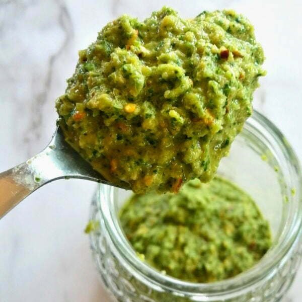 A spoonful of green mojo sauce sits above a jar of green mojo sauce