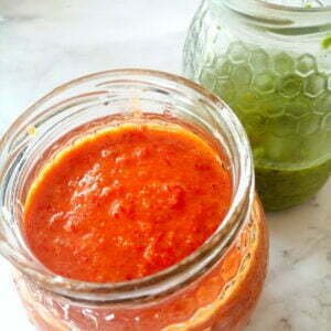 Two jars of red and green mojo sit on a counter top.