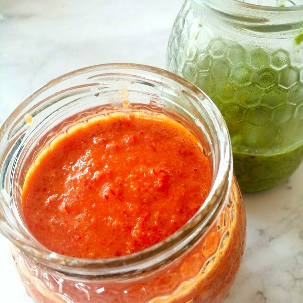 Two jars of red and green mojo sit on a counter top. 