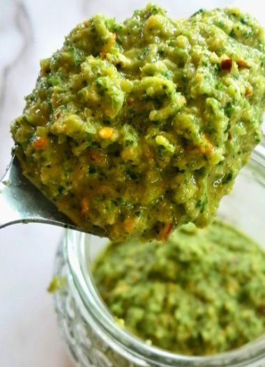 A spoonful of green mojo sauce sits above a jar of green mojo sauce