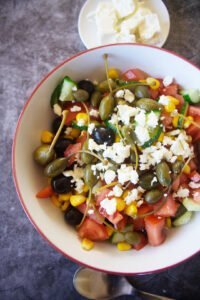 salad ingredients are mixed in a large red bowl.