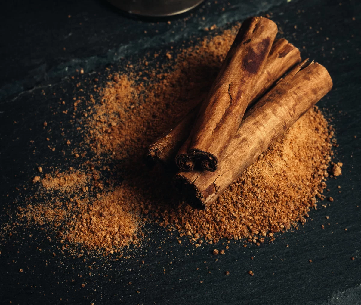 a few sticks of cinnamon sit on top of a pile of ground cinnamon