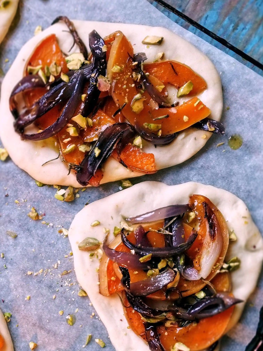 Spanish cocas sit on an oven tray with pumpkin and caramelized onion topping