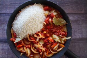 rice is added to pan of sauteed vegetables and tomato