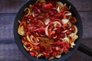 Diced tomato are added to a pan of fried vegetables and spices