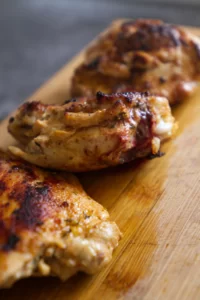 cooked chicken fillets sit on a chopping board.