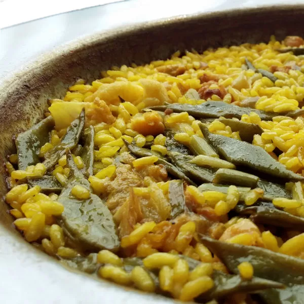 A large pan of paella Valenciana sit garnished with green beans, chicken and pieces or stewed rabbit.