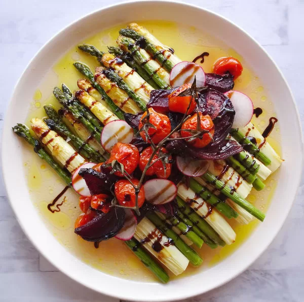 a plate of seasonal roast veggies sits on a white plate in some sauce