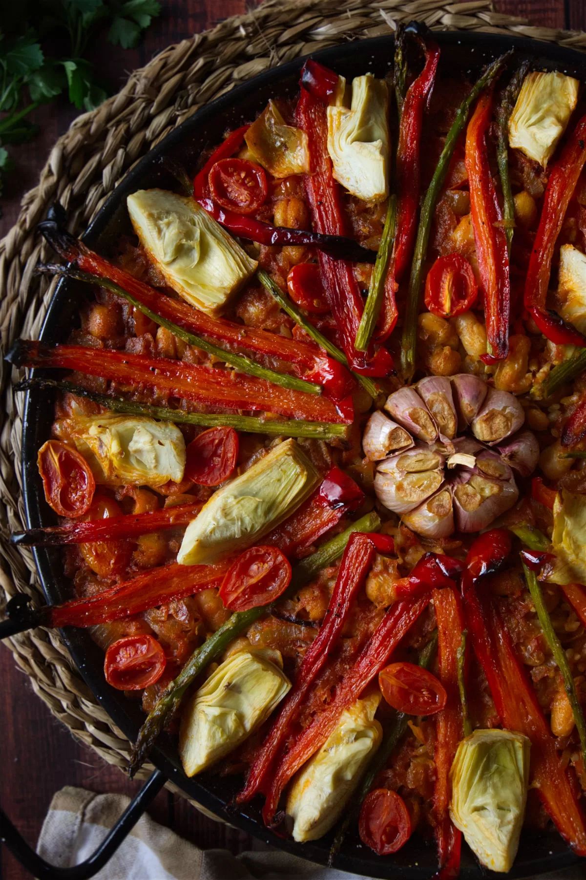 a large pan of vegan arroz al horno is topped with roasted red pepper and a whole head of garlic