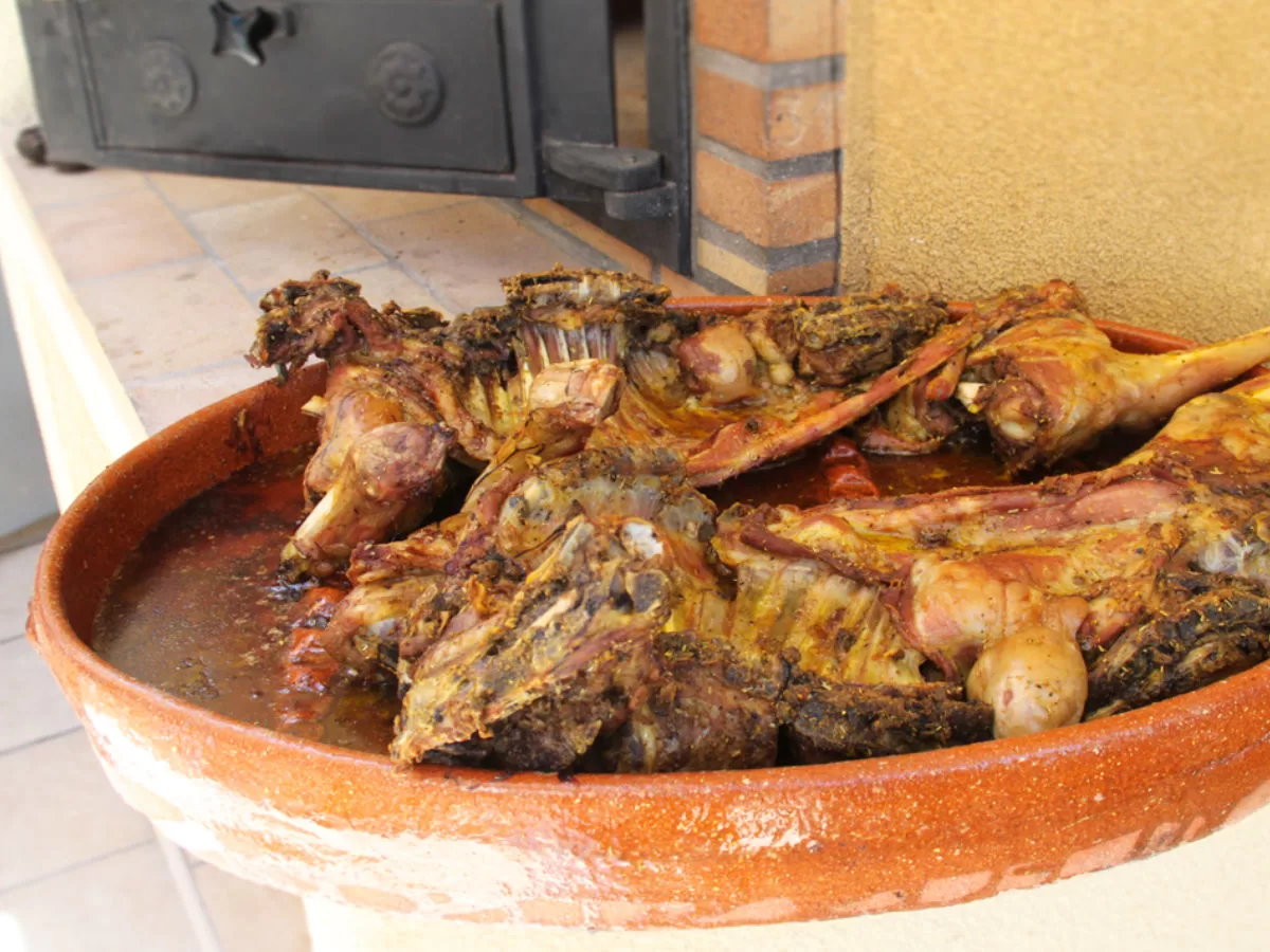 A large earthenware dish is piled with hunks of roast lamb. 