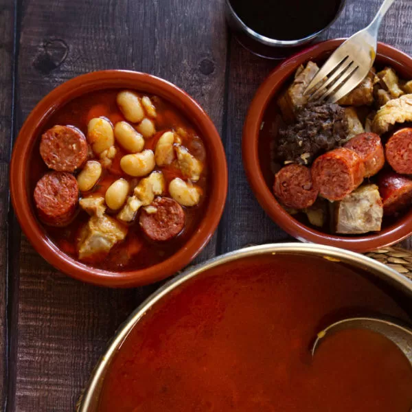 a small bowl of Fabada Asturiana is served from a large steaming pot.