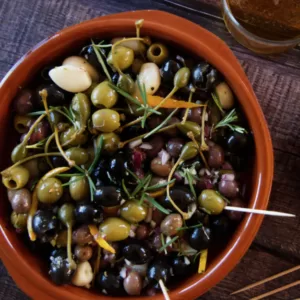 a small earthenware dish filled with mariated olives Spanish style.