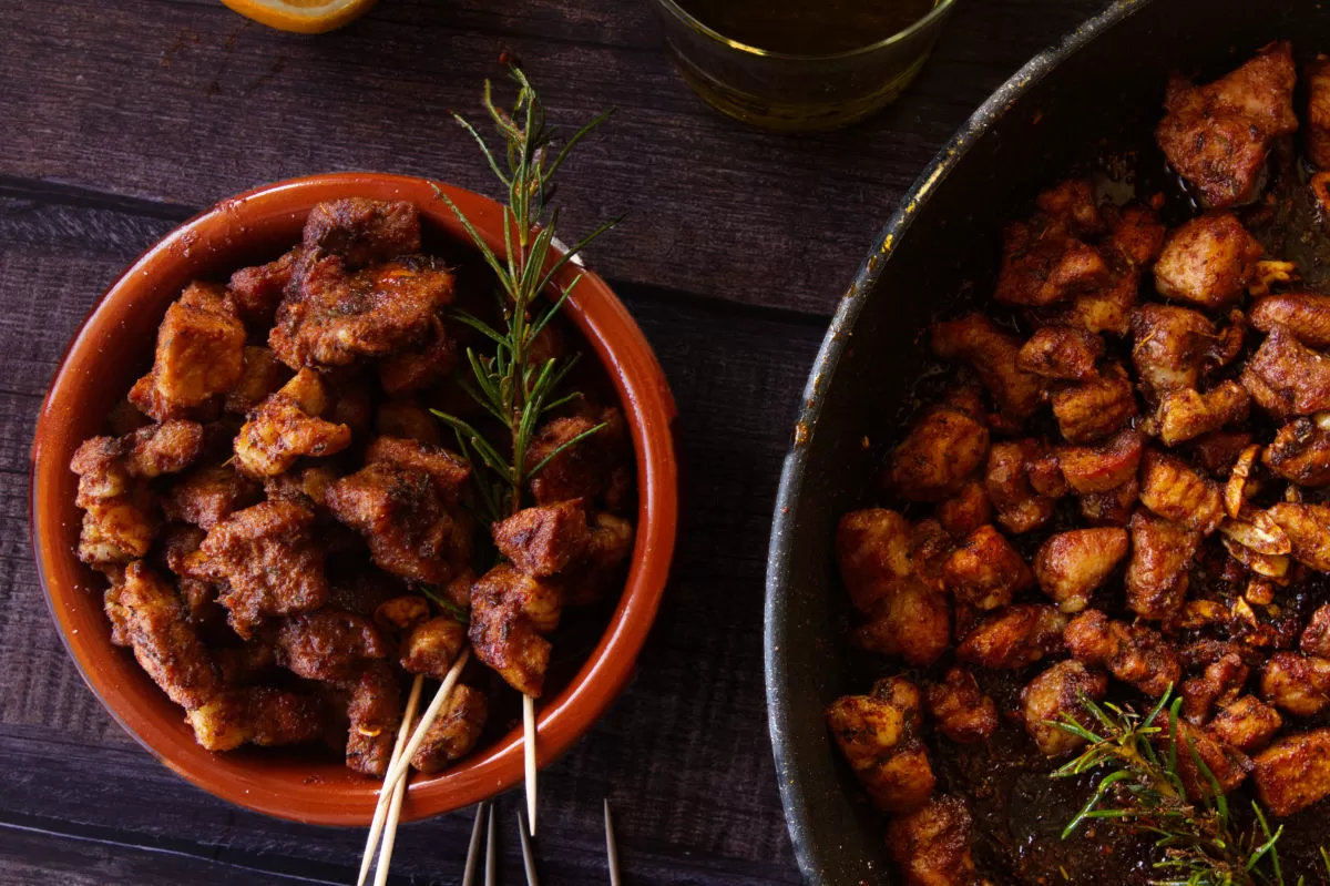 a small bowl of paprika-infused pork bites sits next to. alrge fry pan of cooked pork. 