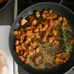 rosemary and some slicced garlic are added to a pan of fried pork