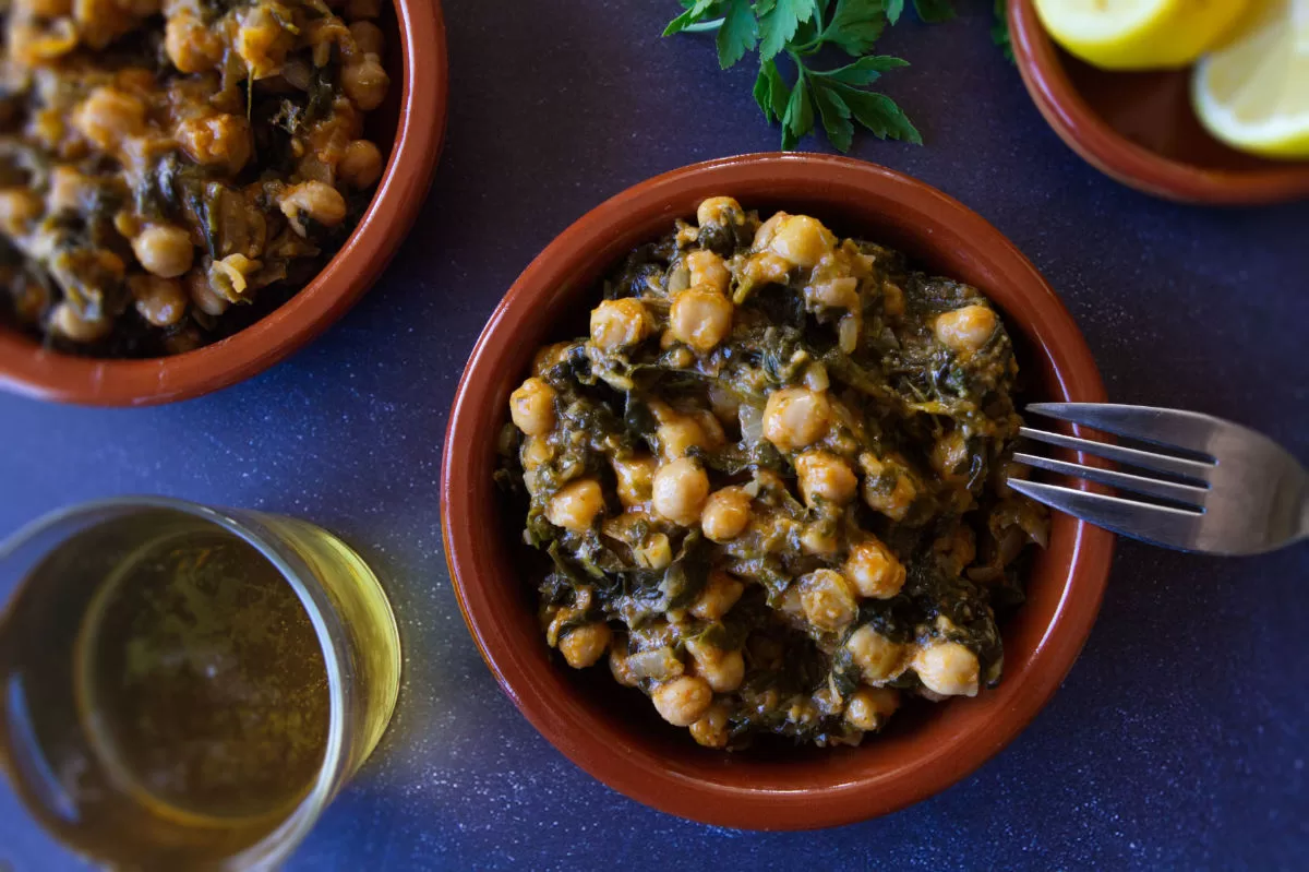 a few small bowls spinach with chickpeas sits beside some fresh parlsey and lemon wedges.