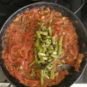 Some roasted asparagus spearss are added to a pan of sauteed sofrito sauce