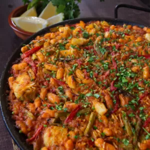 A large pan of Spanish oven-baked rice is garnished with fres hchopped parsley