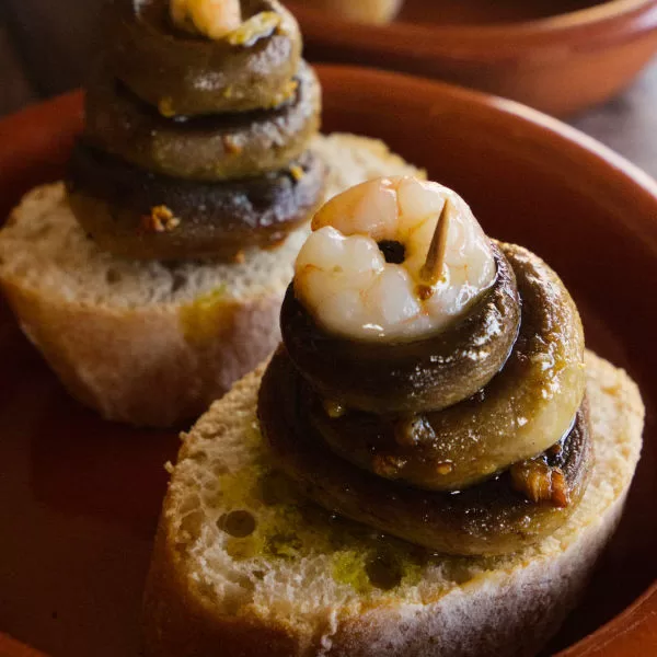 Mushrooms and shrimp tapas are served in a small earthenware bowl