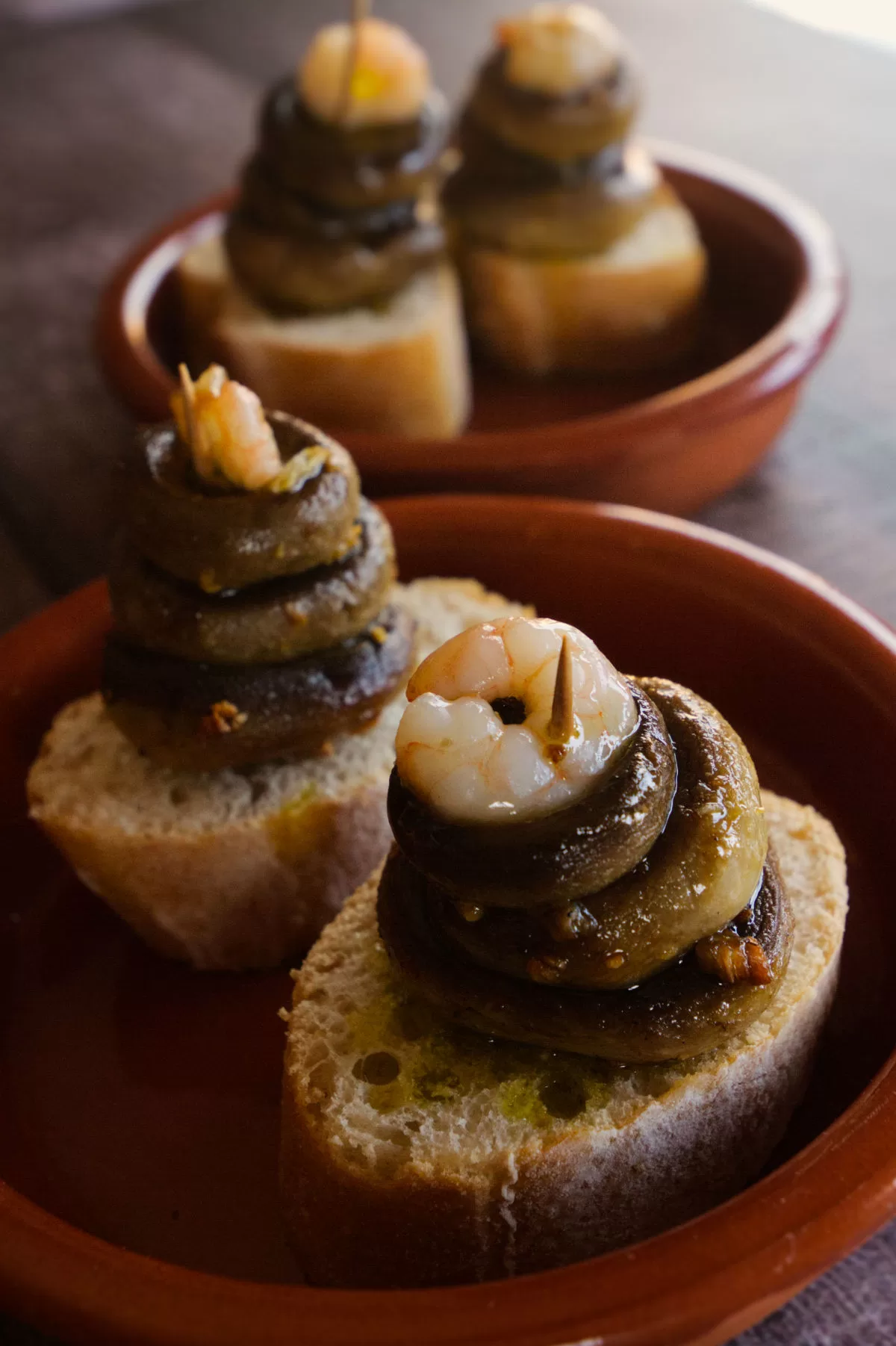 2 small bowls of mushrooms and shrip tapas sit on a wooden benchtop