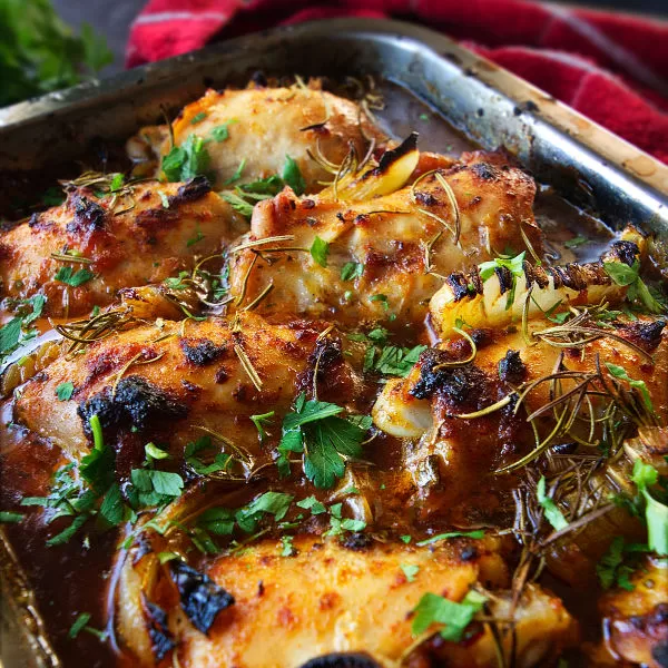 a baking tray full of bbaked Mediterranean chicken thighs