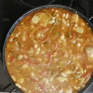 Stock is added to a large pan of sauteed veg.