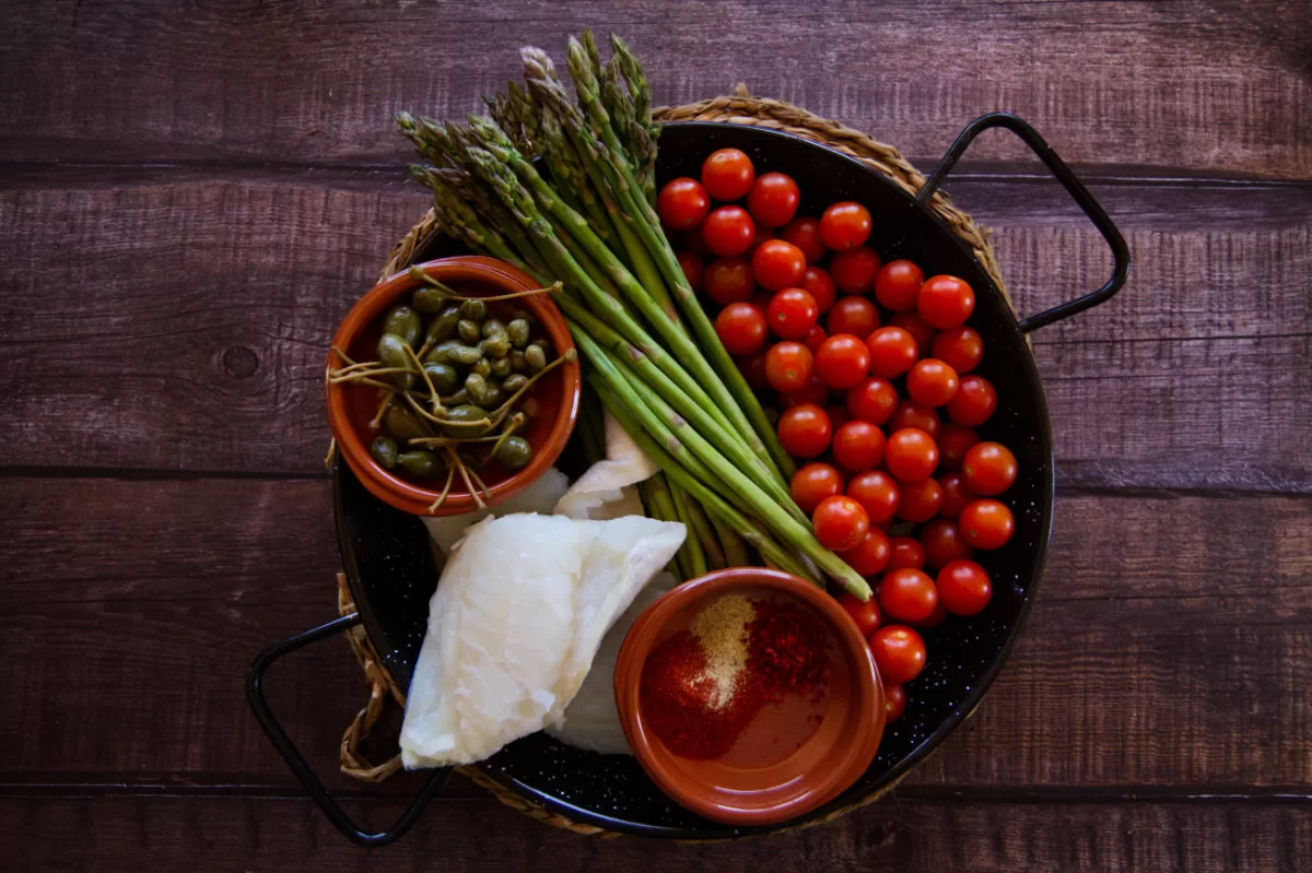 ingredients for making oven-baked codfish are laid out in a alrge paella pan.