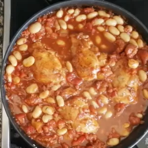 A large pan of chicken and beans simmer in a red sauce.