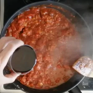 A glass of red wine is added to a rich red sauce.