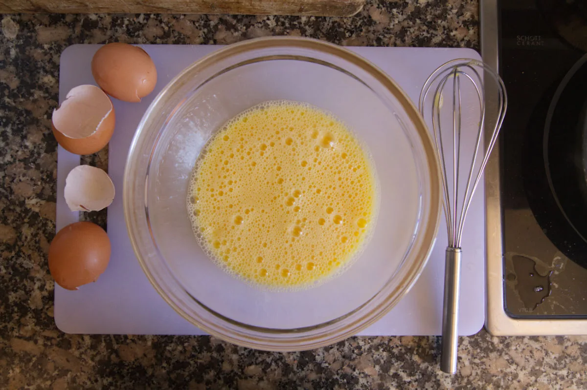 Eggs are whisked in a clear glass bowl.