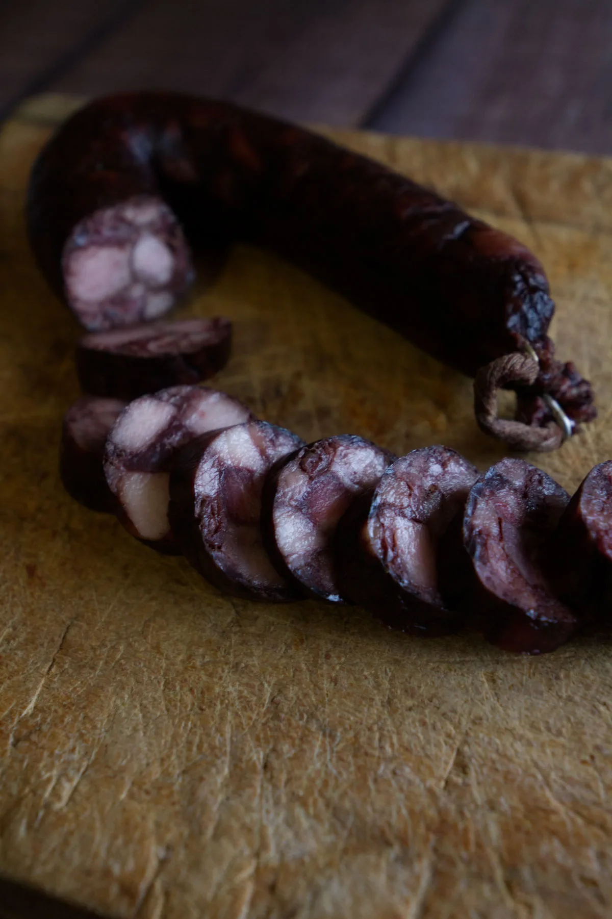 A dark sausage sits sliced on a chopping board. 