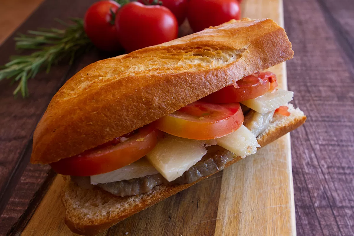 A pork loin sandwich is loaded with some cheese slices and tomato. 