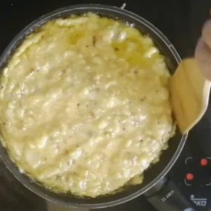 A spatula losens the edges of a tortilla cooking in a frying pan.