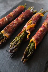 Roasted asparagus spears wrapped in Serrano ham sit on a slate plate.