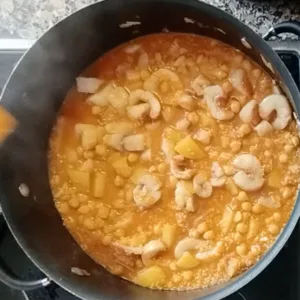 Some chunks of fish are added to a large pot of fish stew.